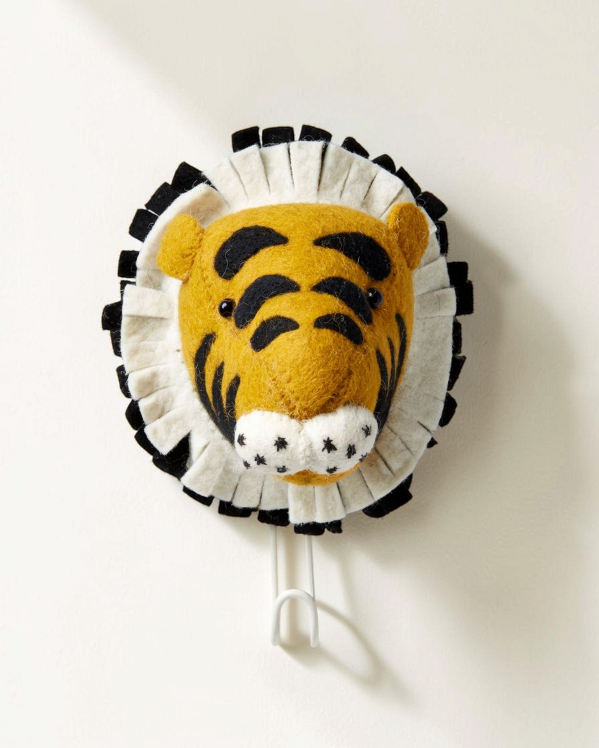 Sprall väggkrok formad som ett tigerhuvud i ekologisk ull med svartvit man, perfekt för barnrummet.