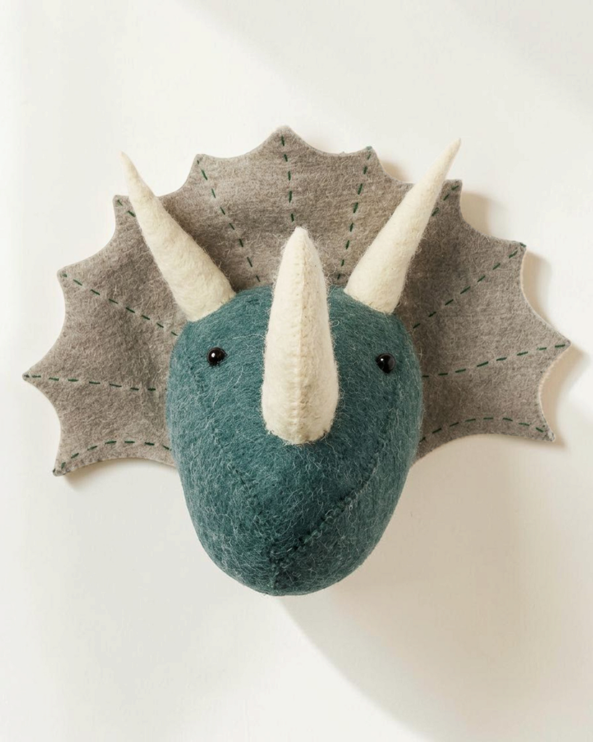 Sprall vägghängt djurhuvud i form av en triceratops tillverkad av ekologisk ull i gröna och beige toner.